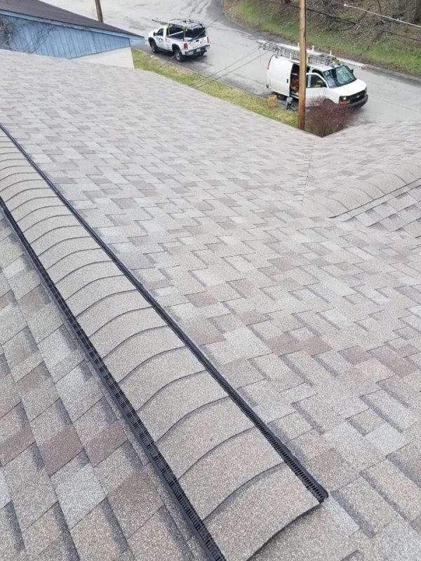 Roof with new shingles and flashing. Two work vehicles parked nearby on the street.