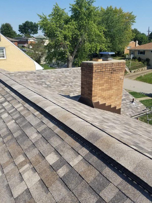 Brown and gray shingled roof with a brick chimney. Bright, sunny day.
