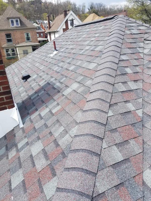 View of a multi-colored shingled roof with a chimney and surrounding buildings.