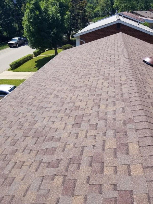 Brown asphalt shingle roof on a house, angled view, sunny day.