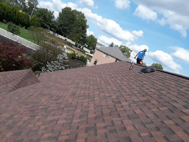 Roofer on a brown shingle roof; blue sky with clouds.