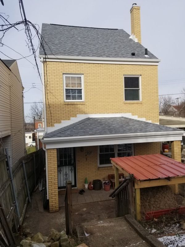 Two-story yellow brick house with gray roof, small porch, and chimney. Overcast day.