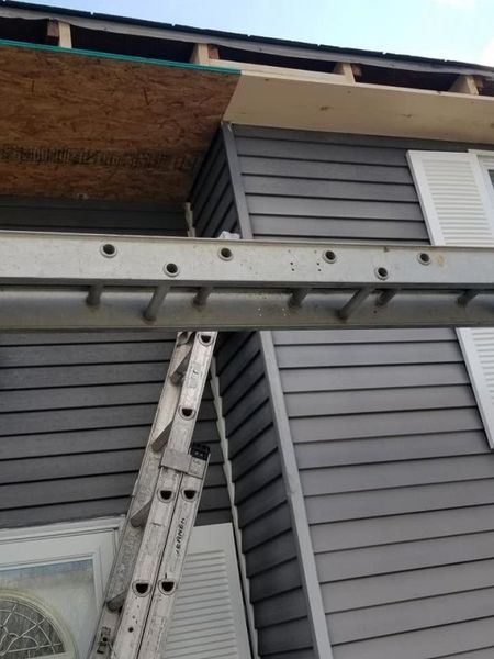 Ladder leaning against a house with gray siding. Construction is visible near the roofline.