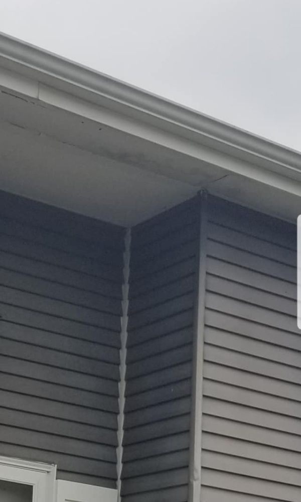 Exterior corner of a building with gray siding, white trim, and a gutter against a cloudy sky.
