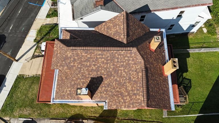 Tan and light brown shingled roof with several vents and a chimney against a green grassy background.