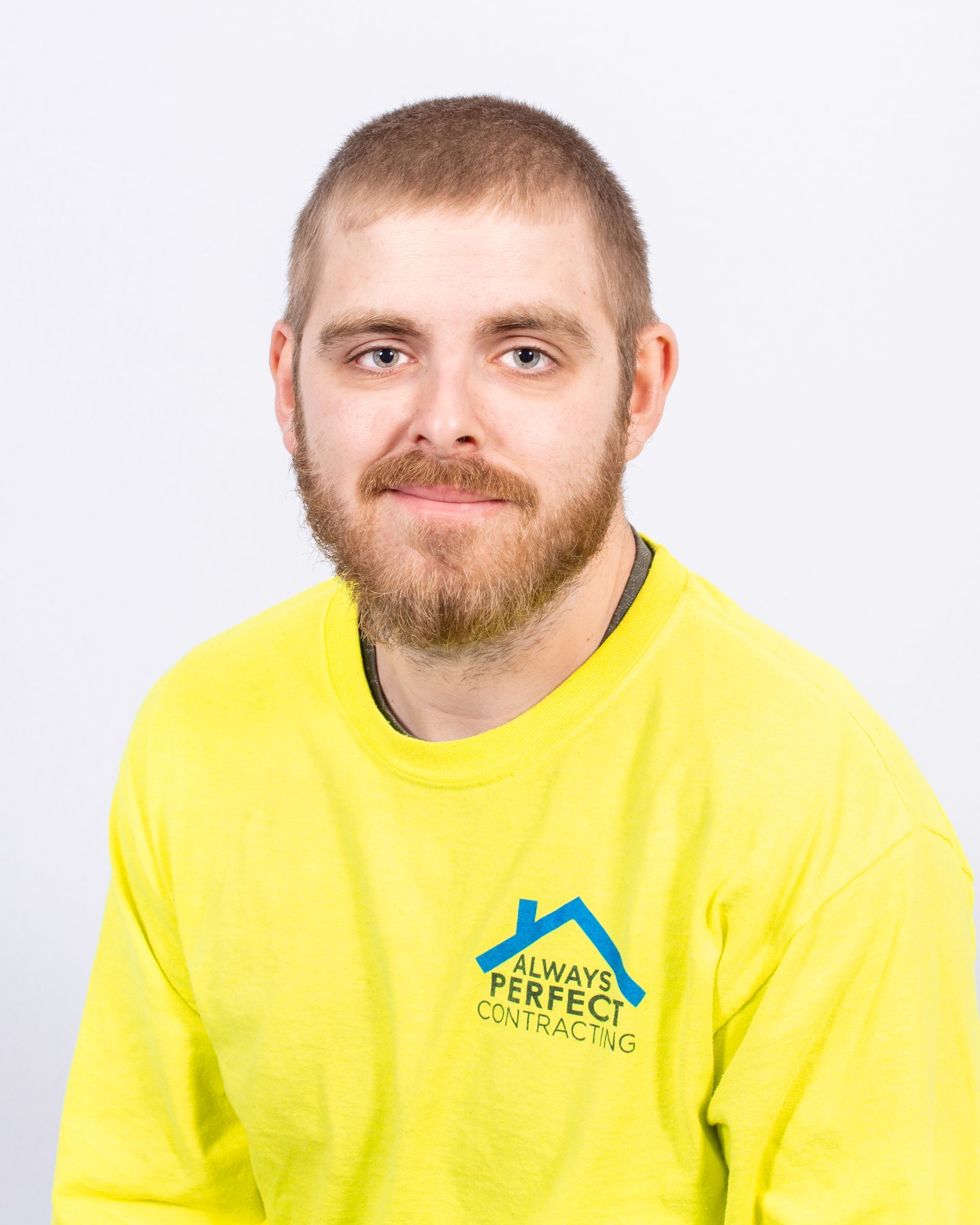 A person with short hair and a beard, wearing a bright yellow long-sleeved shirt with a blue company logo on the chest.