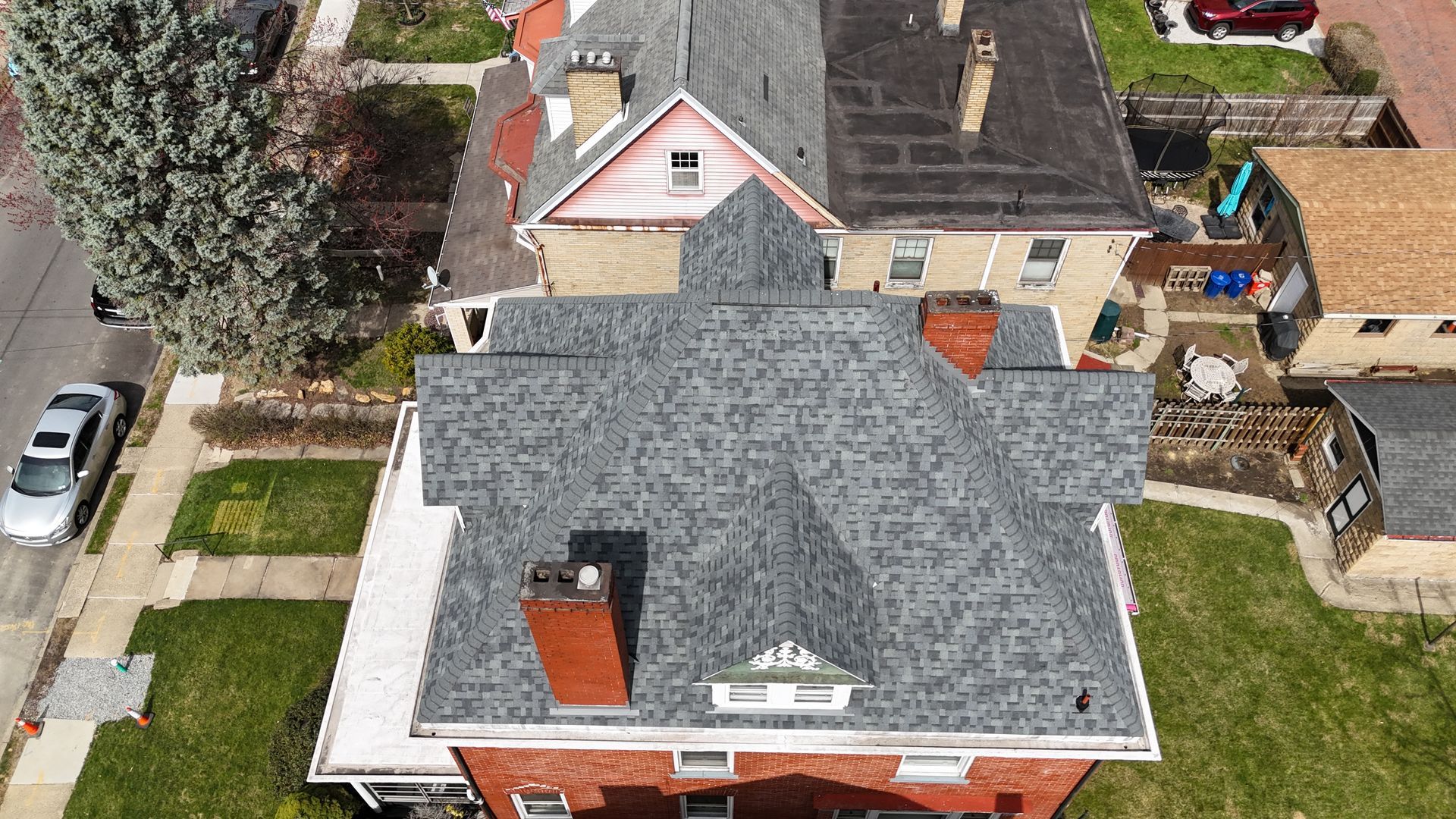 Asphalt shingle roof, angled view. Gray and brown shingles cover the roof with other houses in the background.