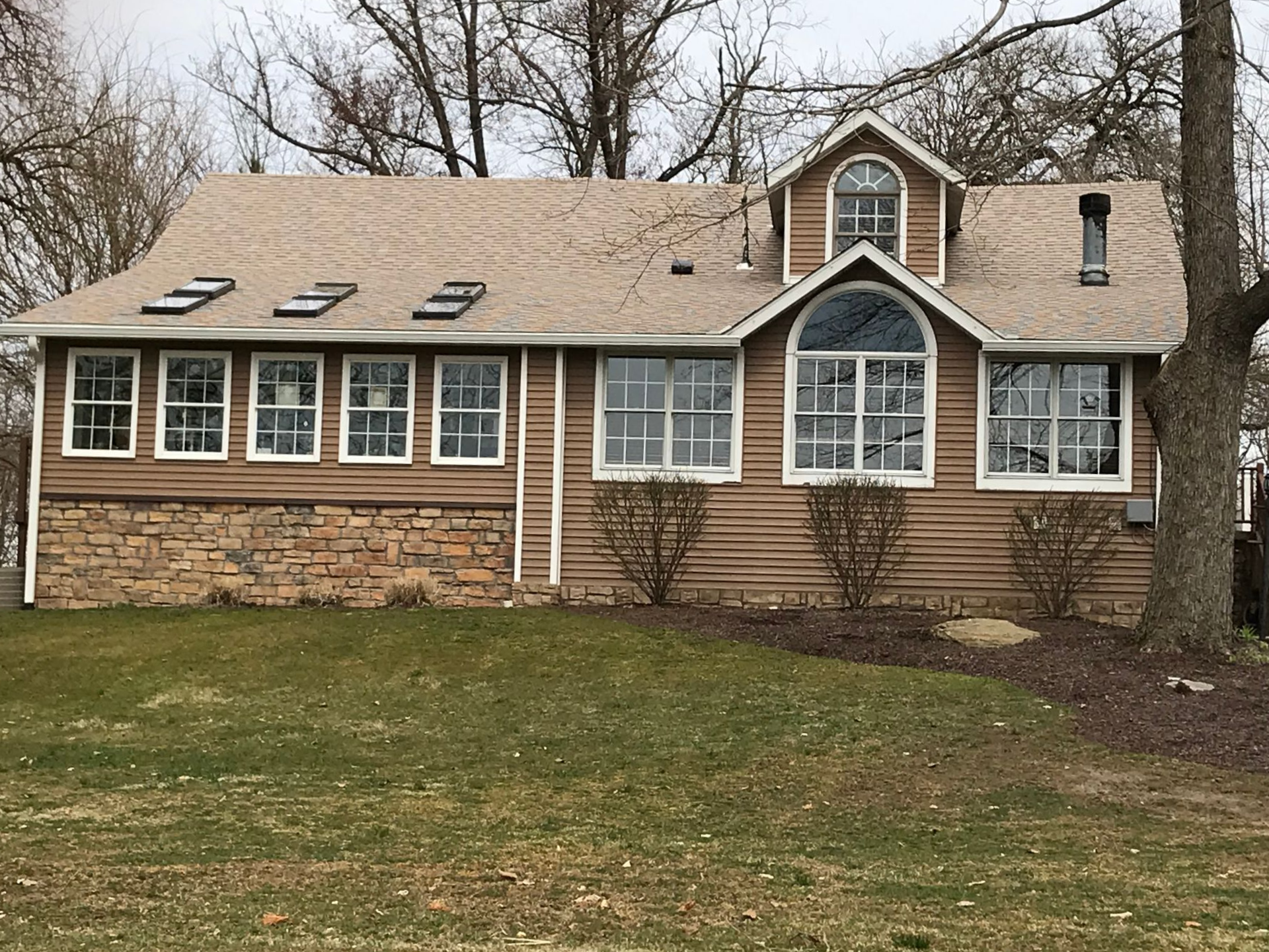 Exterior view of a house. Reddish-brown siding and trim. Stone foundation with a window. Yellow brick wall on the right.
