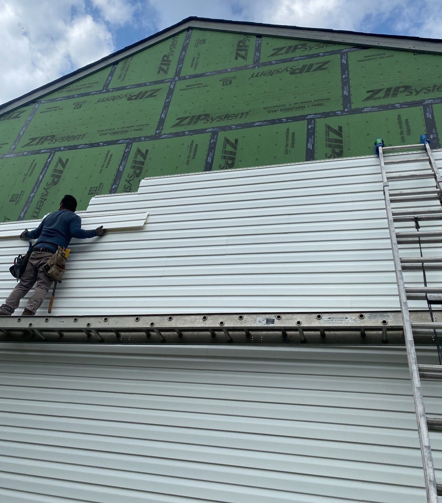 Person on ladder painting exterior of a multi-story brick building.
