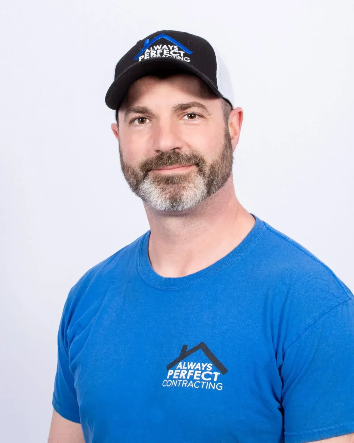 Man in blue shirt and baseball cap with company logo, smiling. White background.