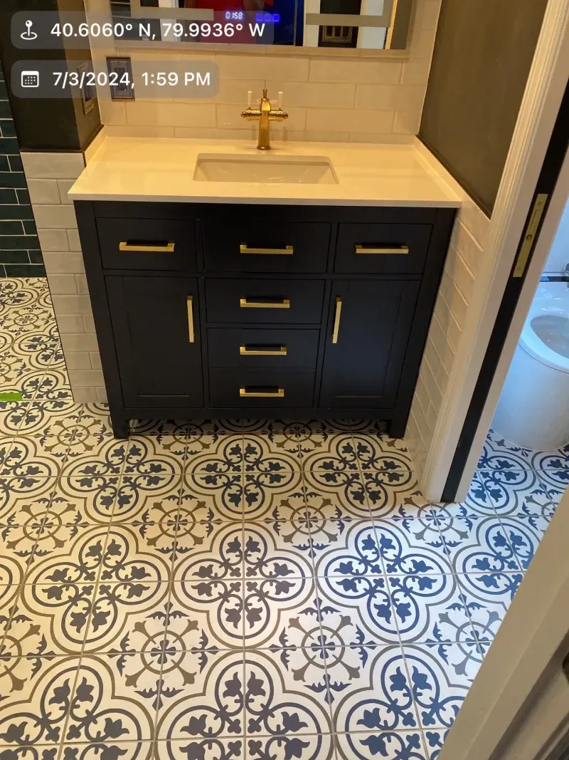 Bathroom with navy vanity, gold hardware, and patterned tile floor.