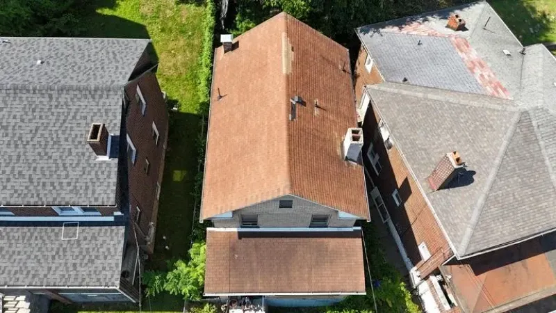 Aerial view of three adjacent houses with pitched roofs and chimneys, set in a green yard.