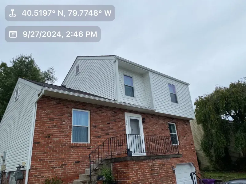Two-story brick house with white siding on the upper level, black railing, cloudy sky.