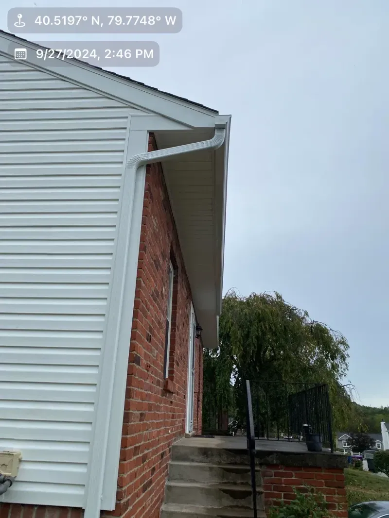 Side of a brick and white vinyl-sided house with a white gutter, under a cloudy sky.