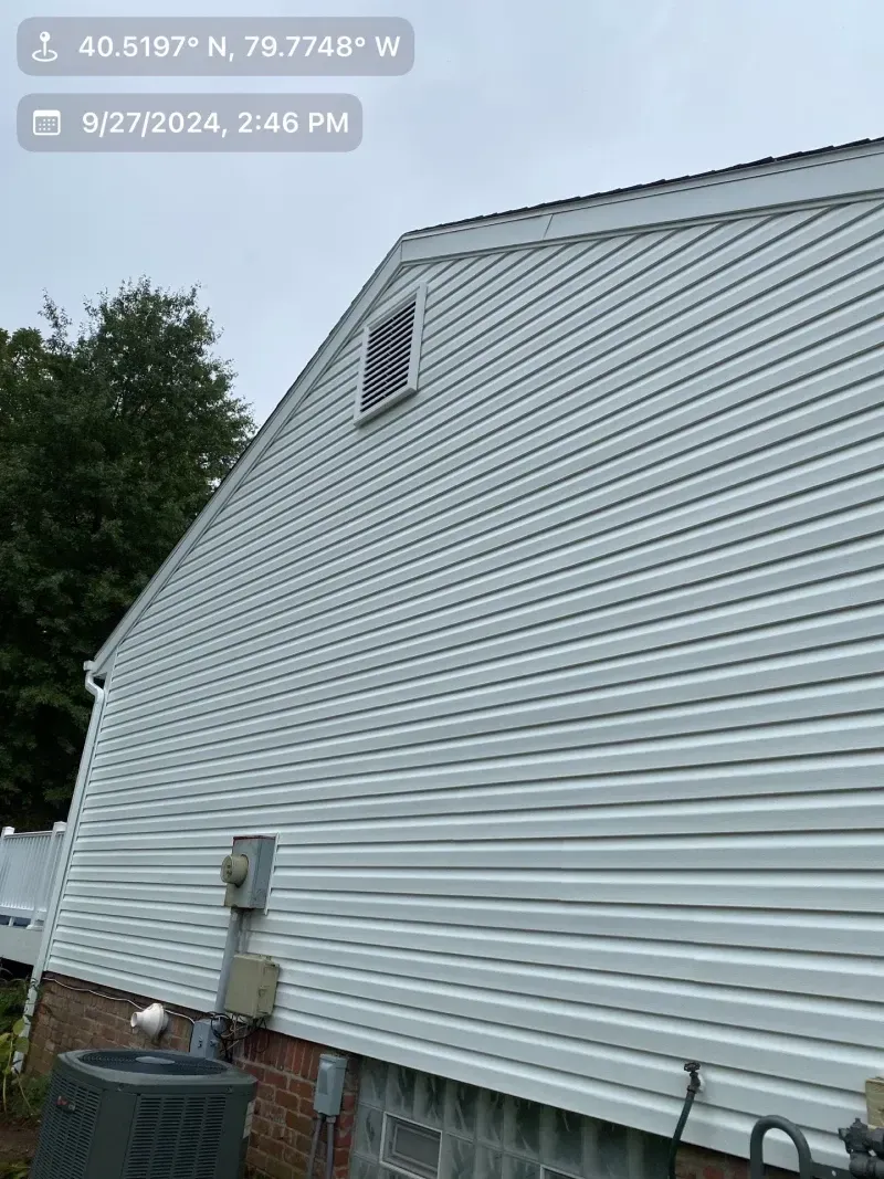 Side of a white-sided house with a vent, surrounded by a cloudy sky and trees.