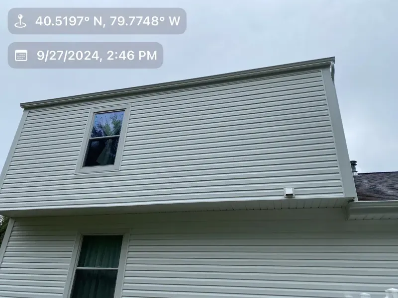 Exterior of a light-colored building with a window in a loft, and the date and coordinates displayed.