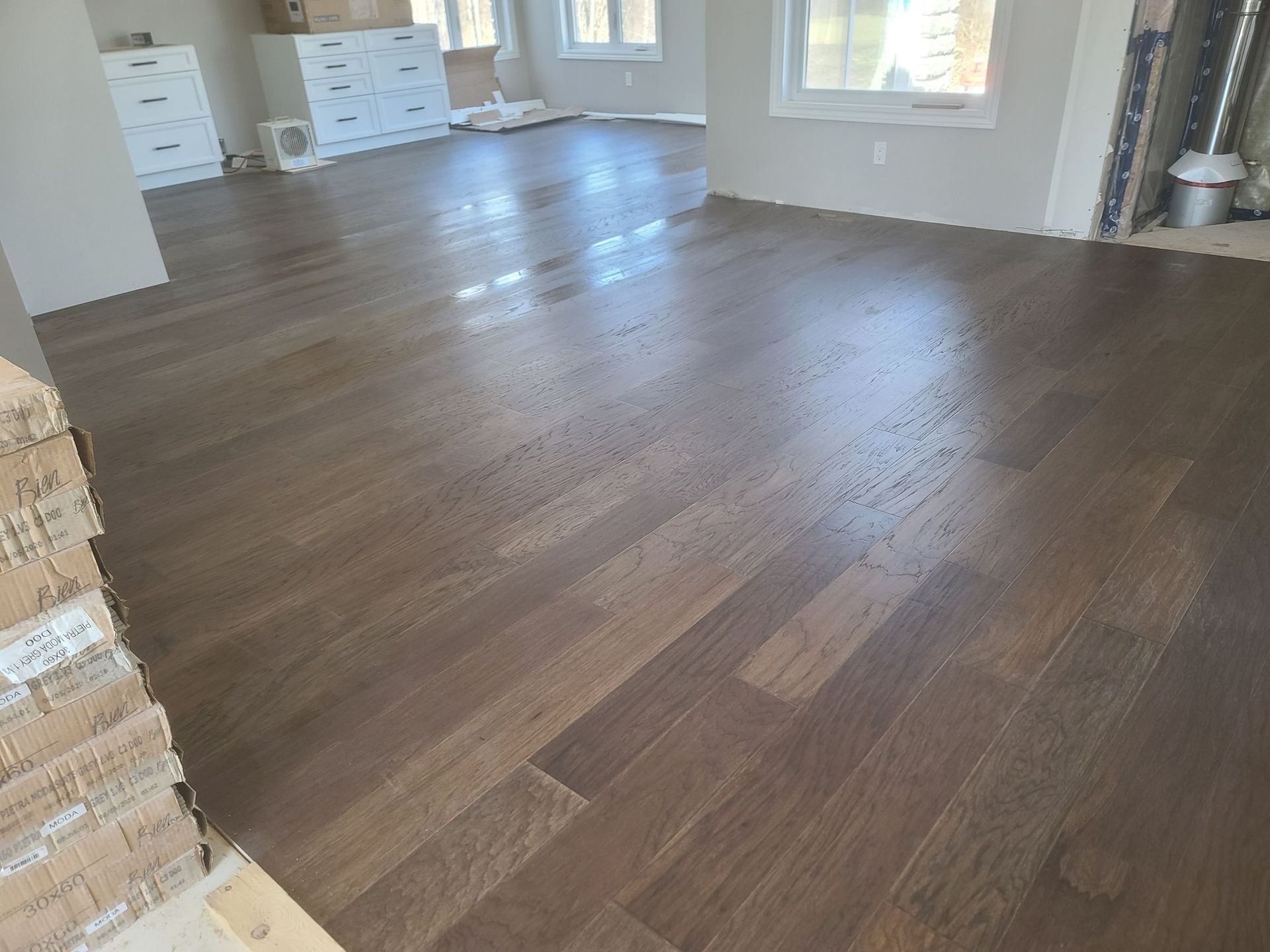A living room with hardwood floors and a stack of boxes on the floor.