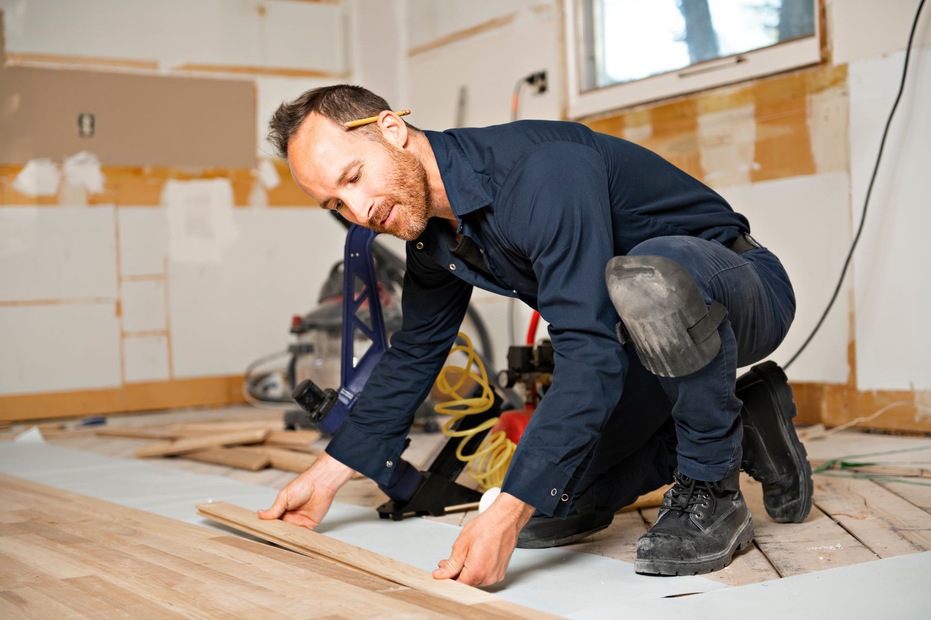 A man is kneeling down to install a wooden floor in a room.