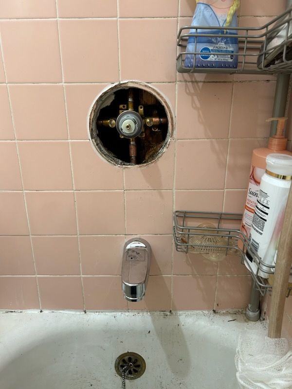 A bathroom with pink tiles and a bathtub with a hole in the wall.