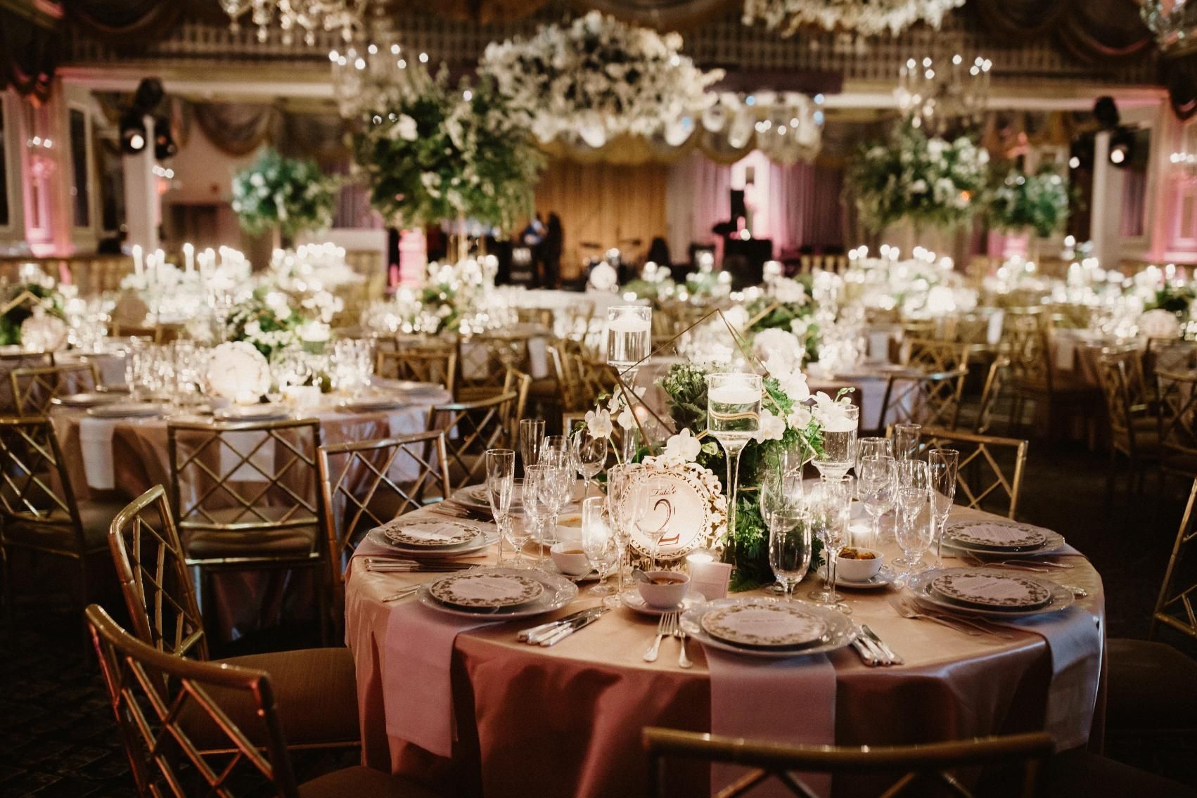 Elegant wedding reception with round tables, floral centerpieces, gold chairs, and soft lighting.