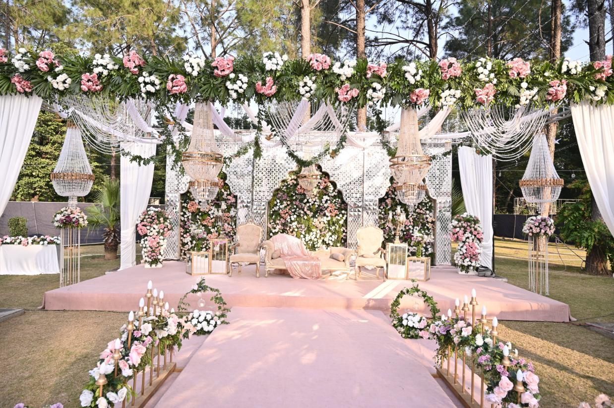 Wedding stage with pink and white flowers, draping, and a pink carpet in a garden setting.