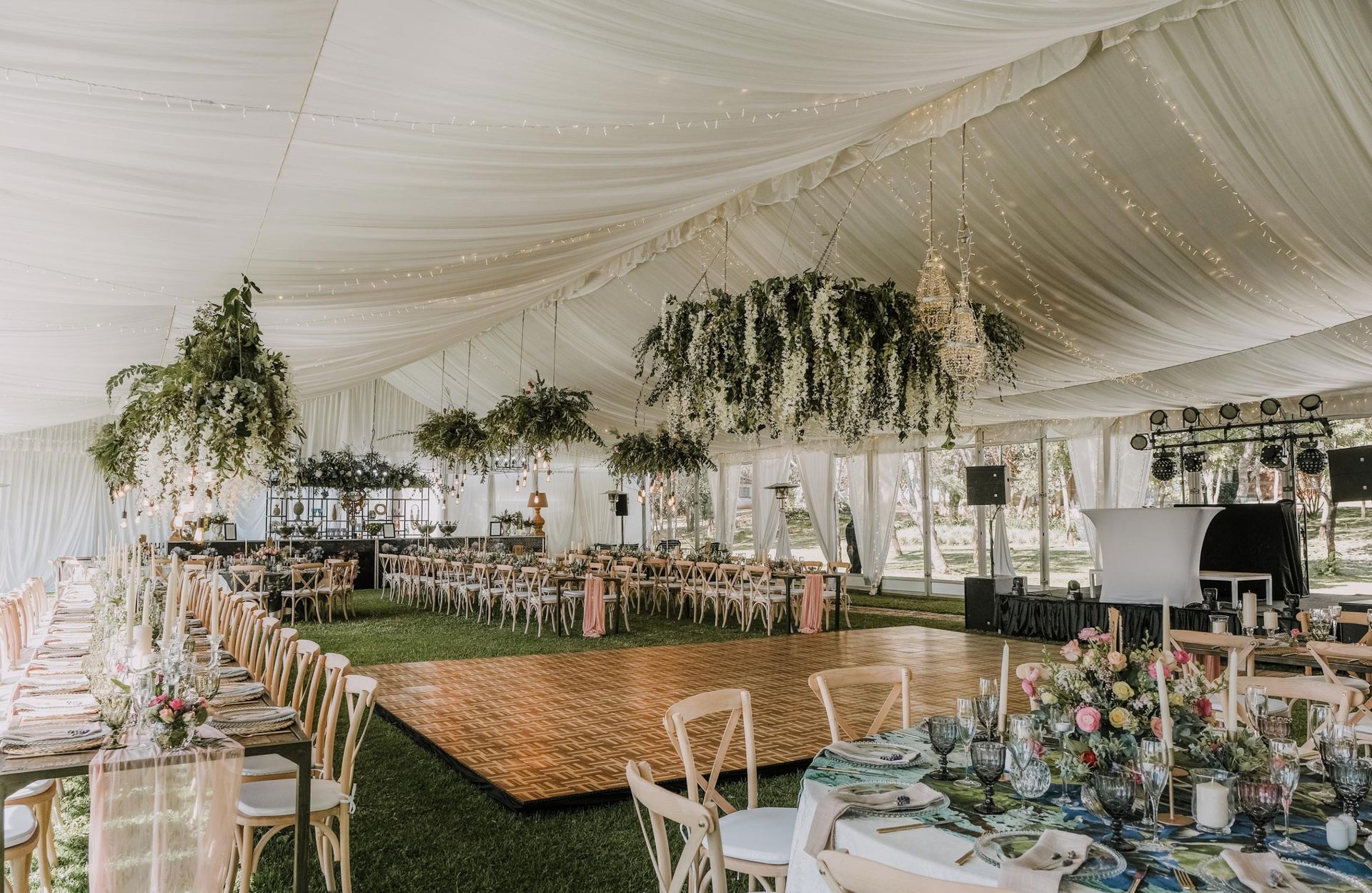 Wedding reception tent, decorated with flowers, tables, and dance floor on grass.