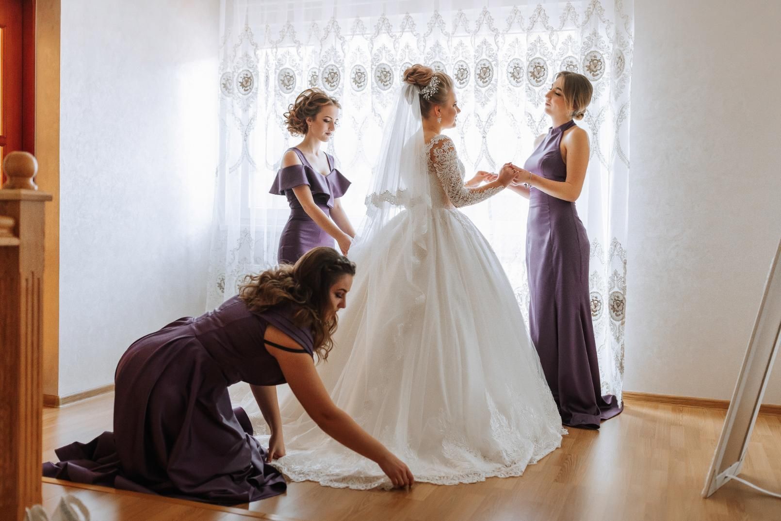 Bride in white dress with bridesmaids in purple, adjusting the gown.