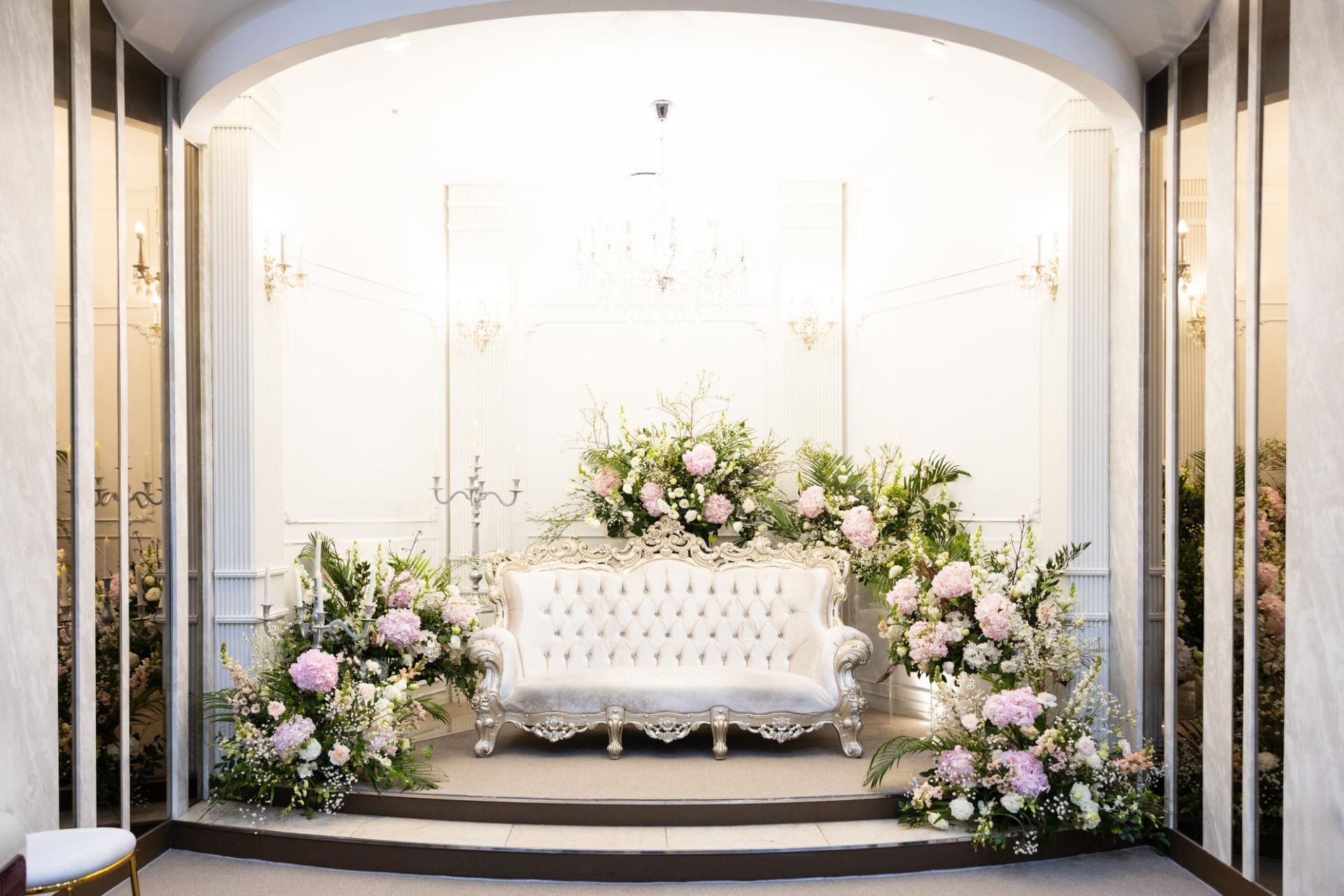 Wedding stage with white couch, floral arrangements, and decorative backdrop.