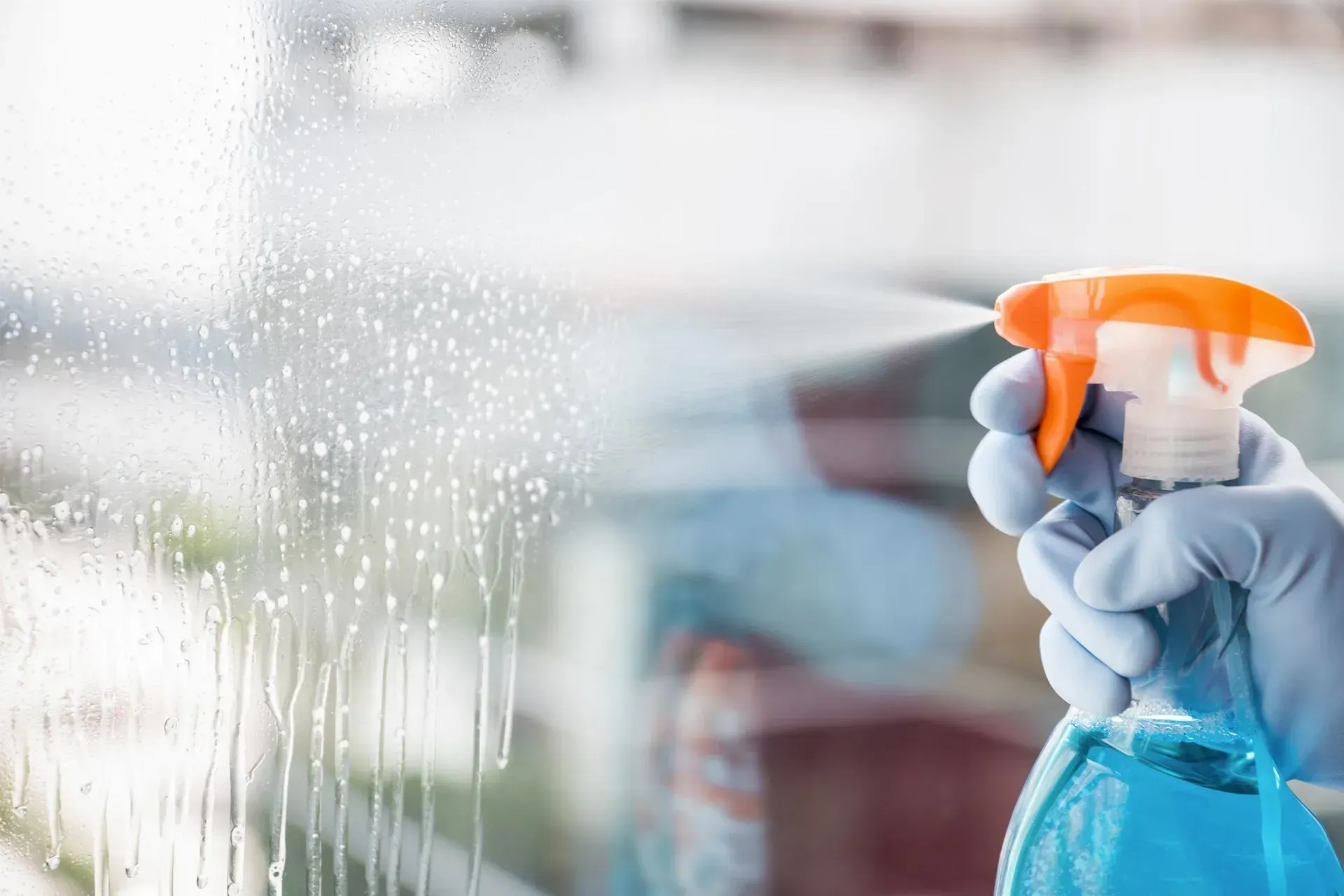 Mano guantata che spruzza detergente blu