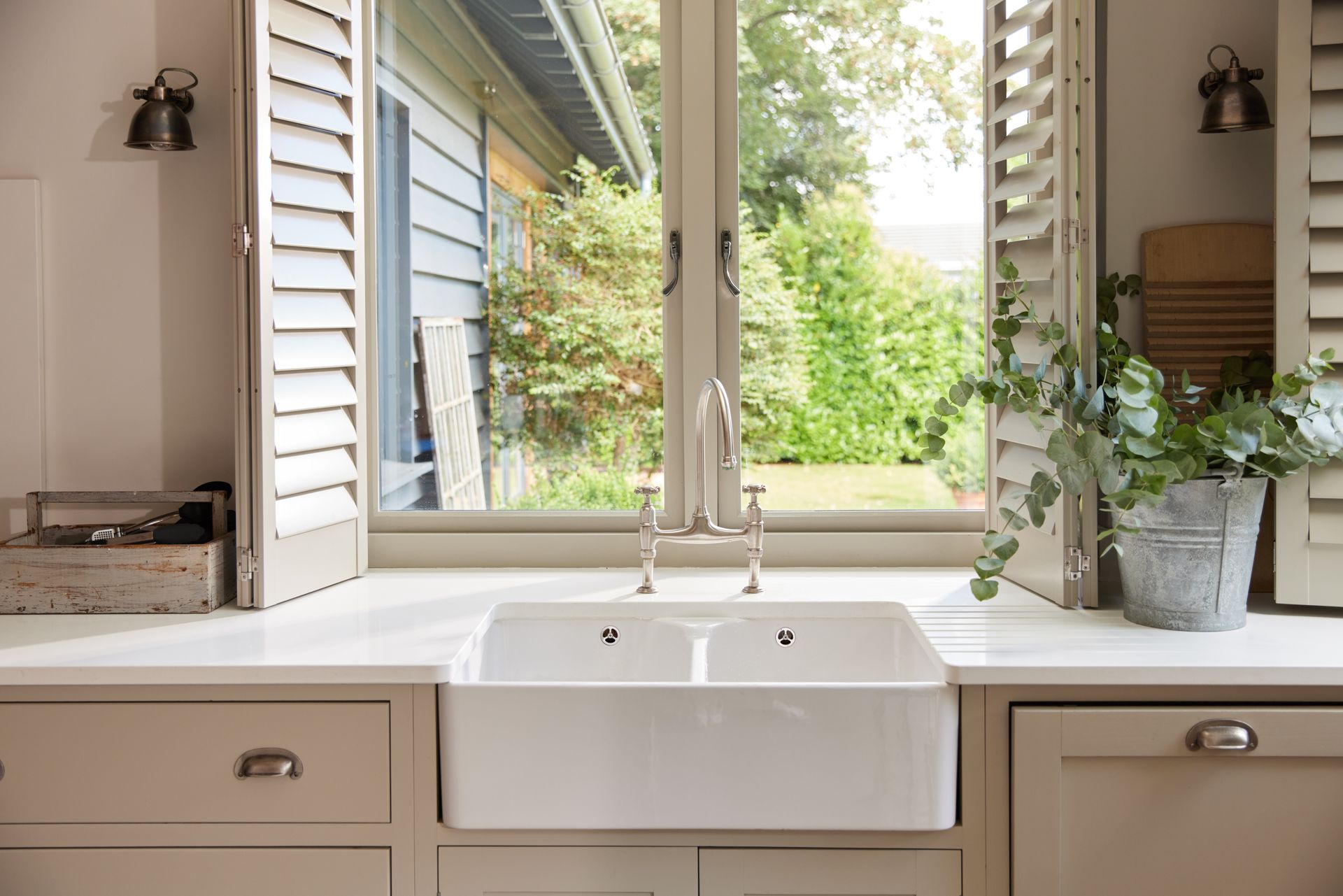Vinyl shutters above a kitchen counter with potted plants and other accessories.