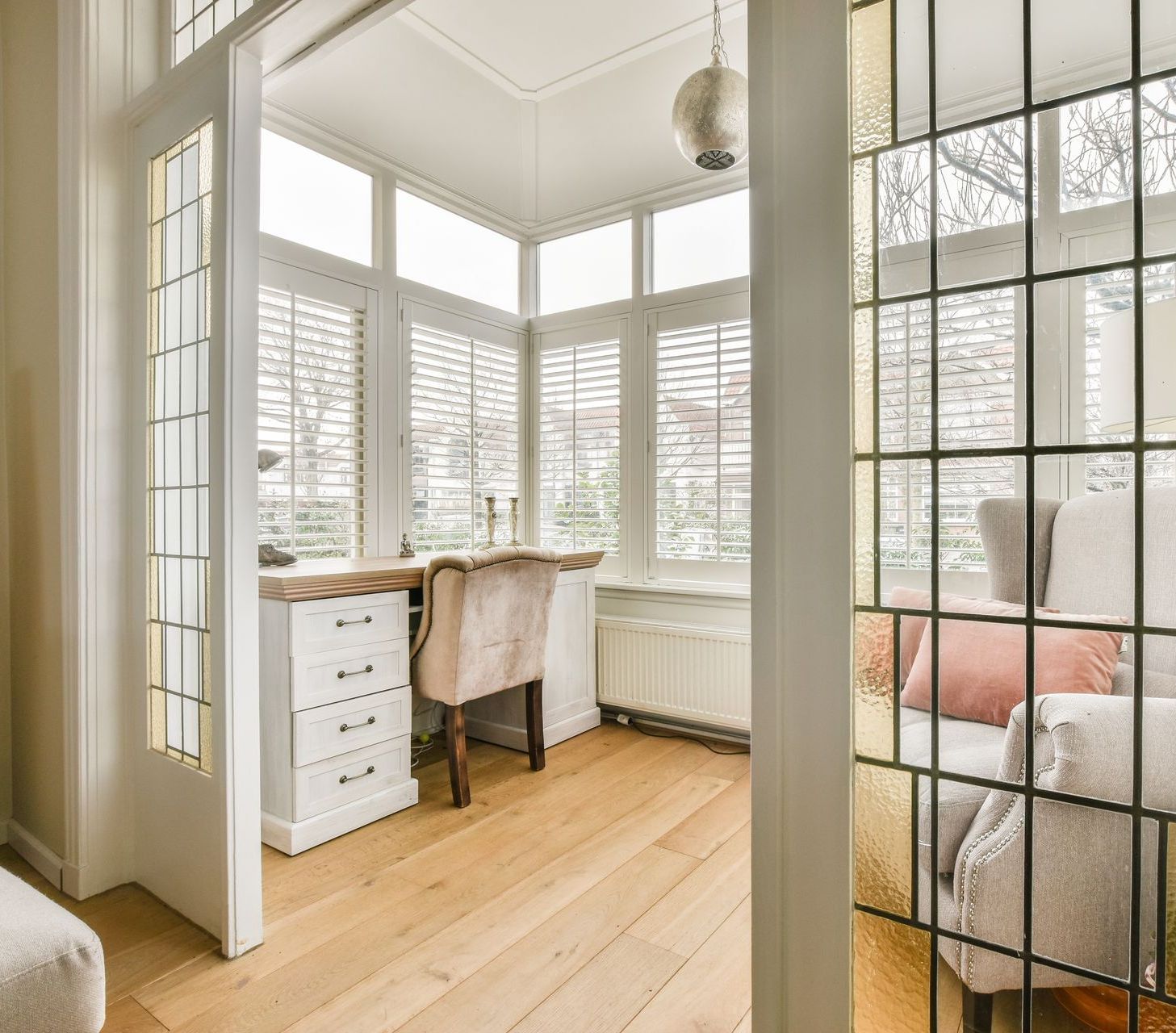 Posh home office with sofa, contemporary desk, and custom white shutters.