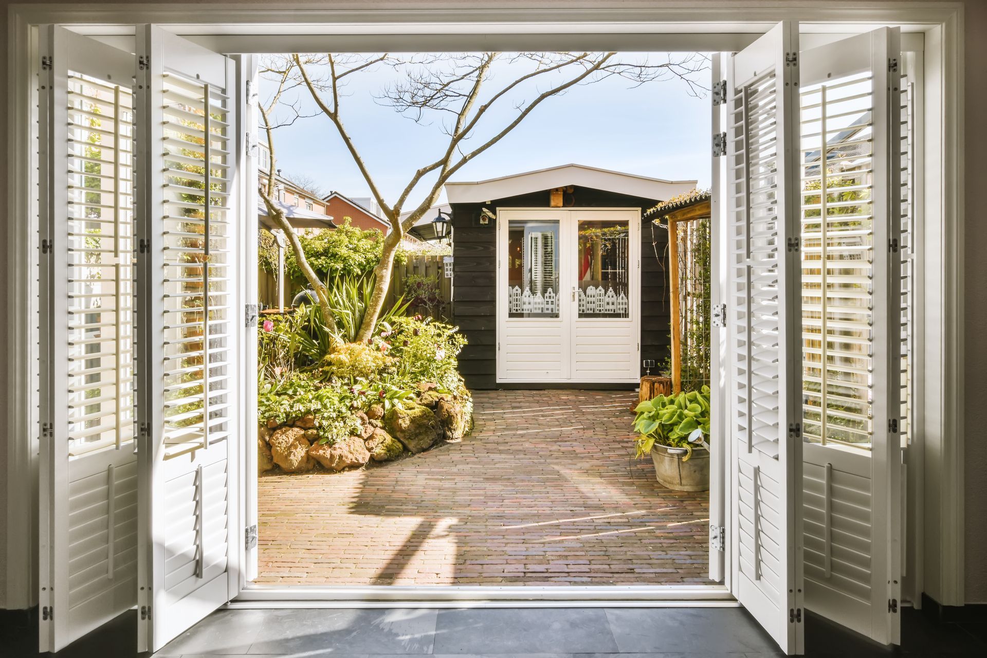 A set of open white door shutters leading into an outdoor garden.