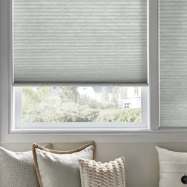 A couch with throw pillows in front of a window with cellular shades.