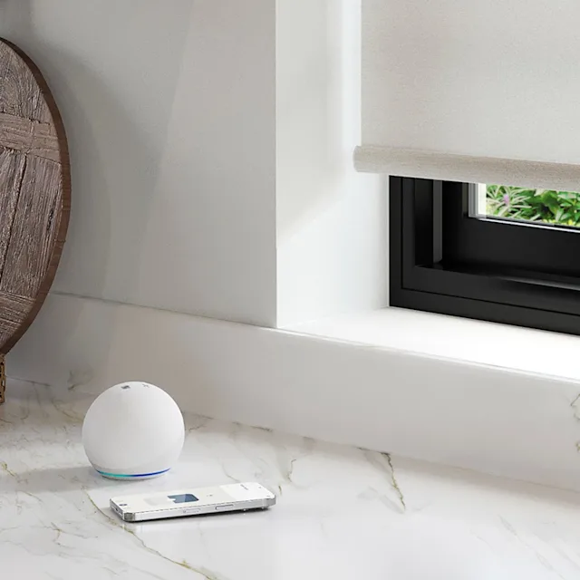 Window treatment remote control beside a smart home device on a counter.