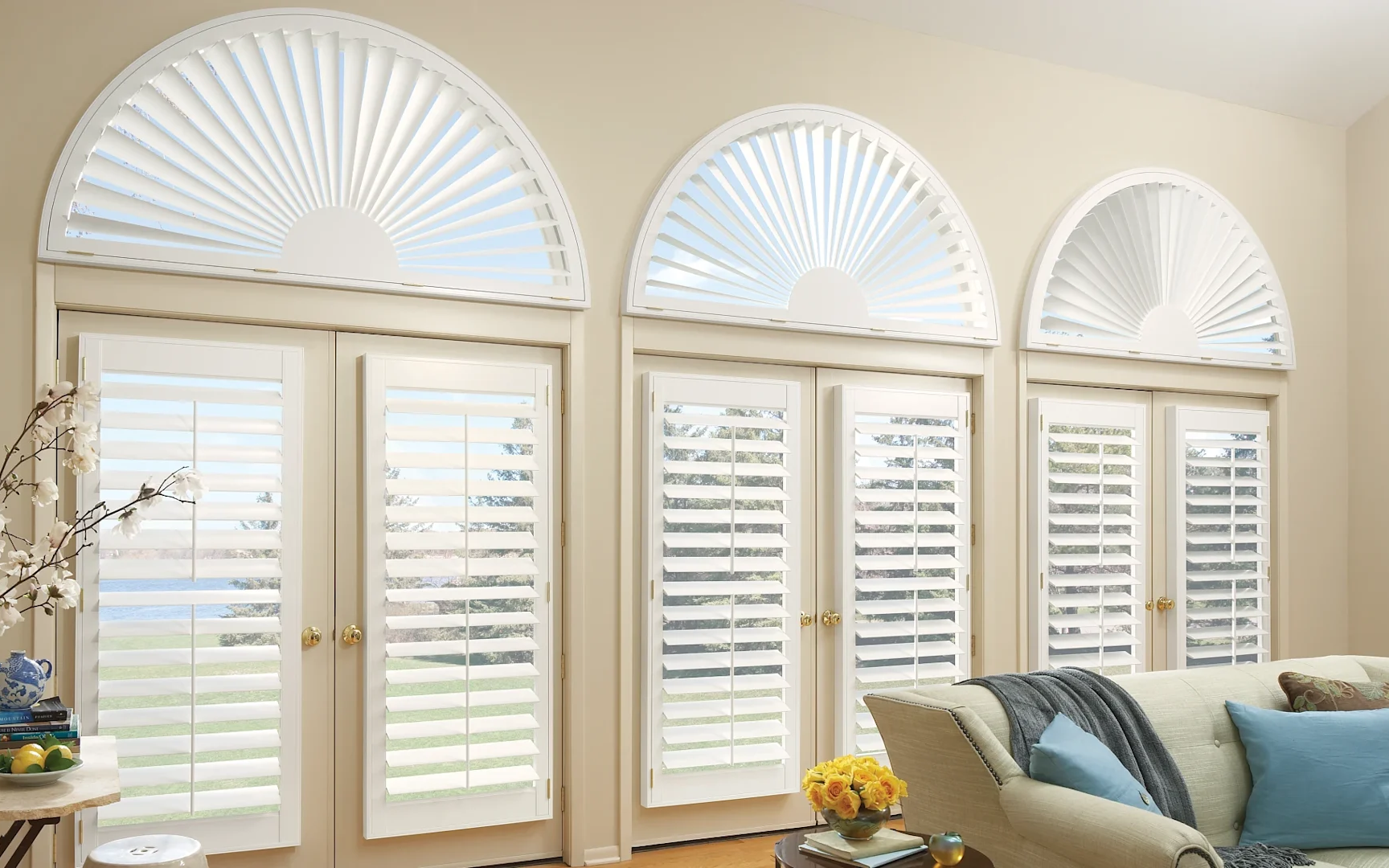 3 arched shutters in a living room managing light in front of a plush sofa and end table.