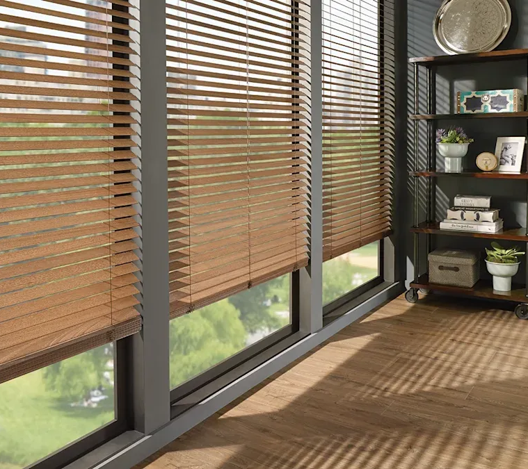 Custom wood blinds covering three windows in a living room with shelving.