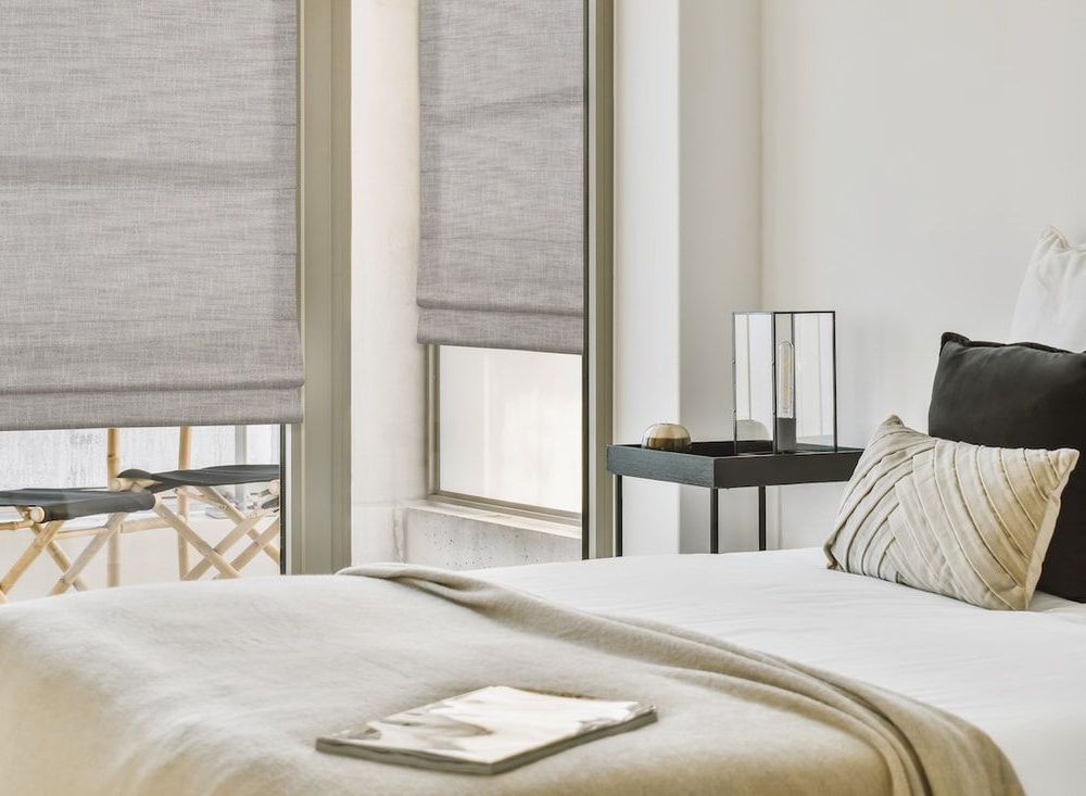 Contemporary bedroom with stylish throw pillows, end table, and custom Roman shades.