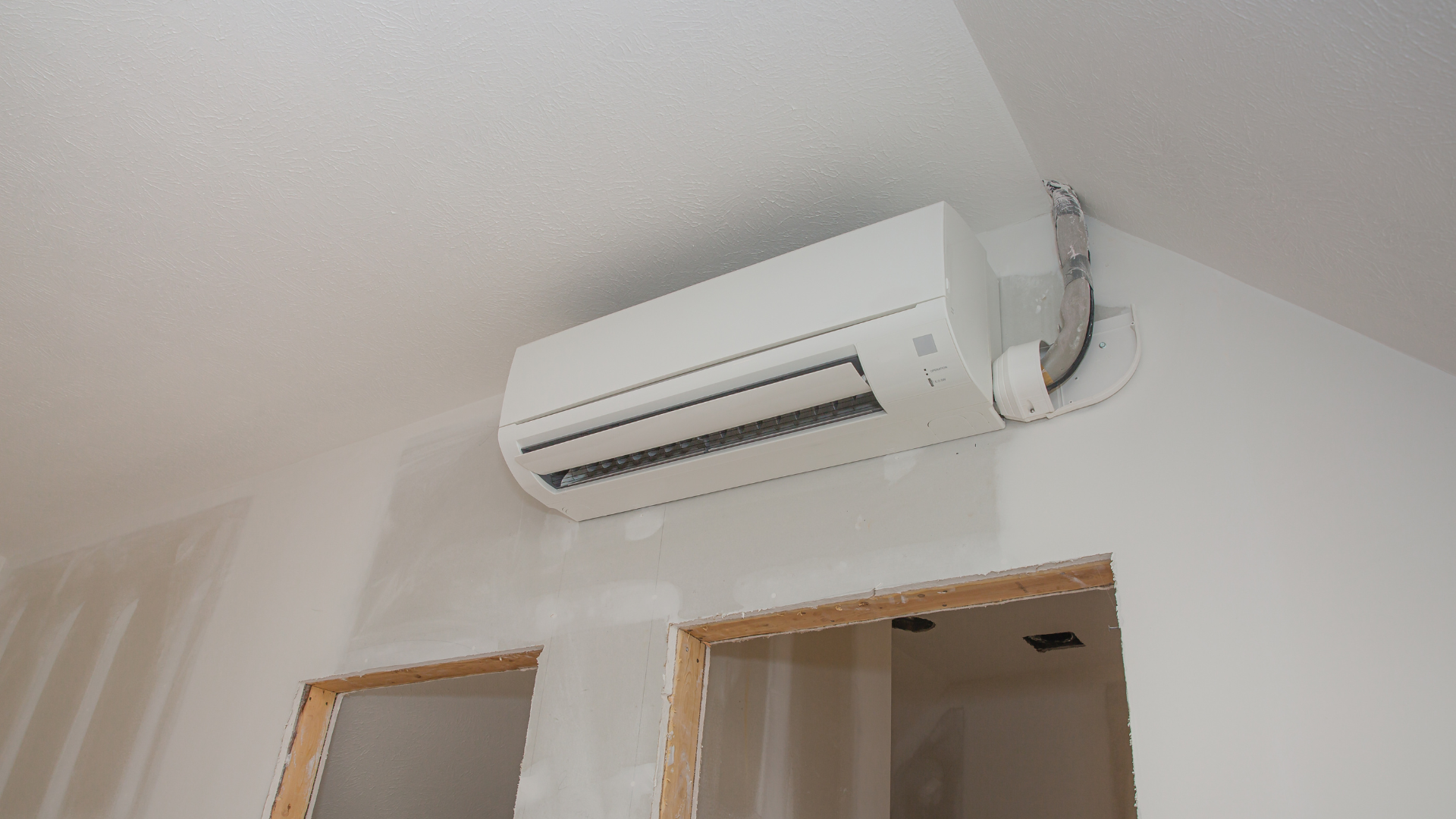 White air conditioning unit mounted on a white wall above a doorway frame.