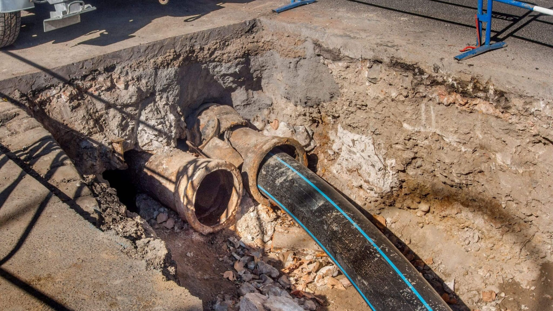 Construction site: Pipes exposed in a hole in the ground; a black hose connected to the pipes.
