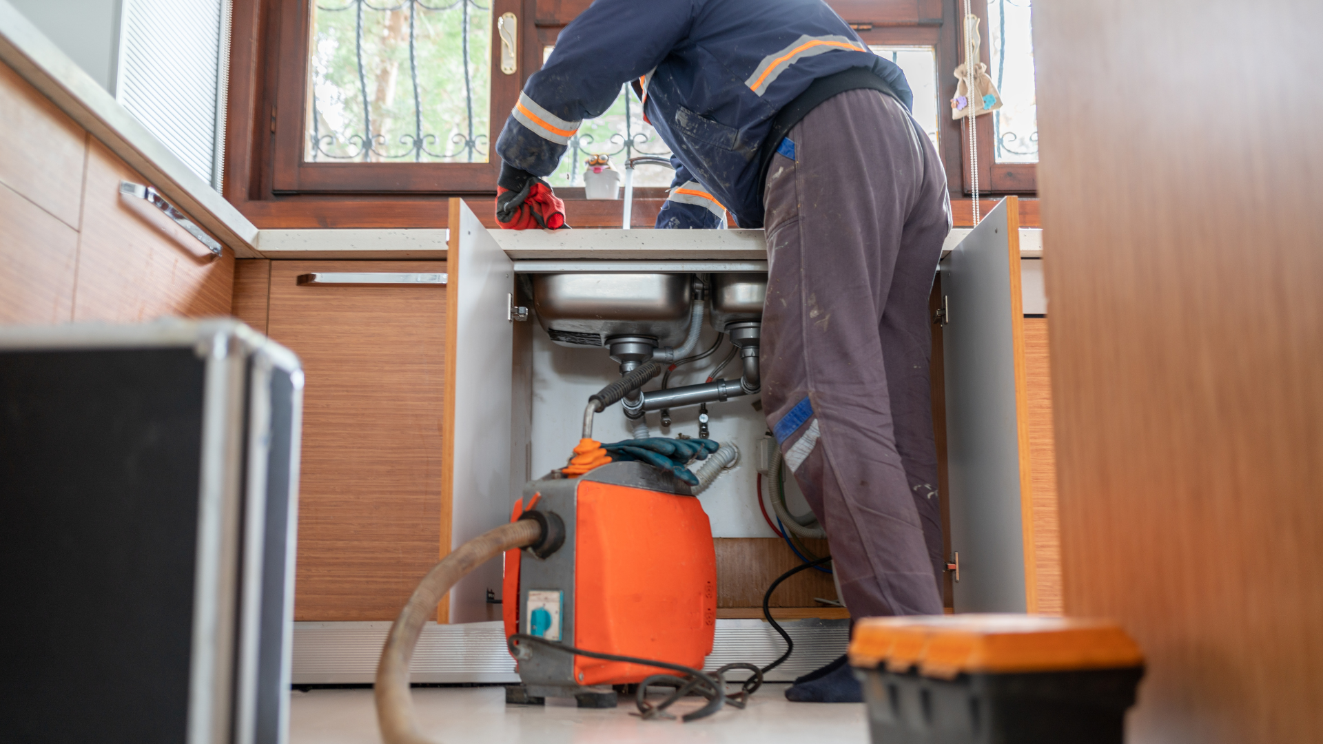 Plumber working under a kitchen sink, using a drain cleaning machine.