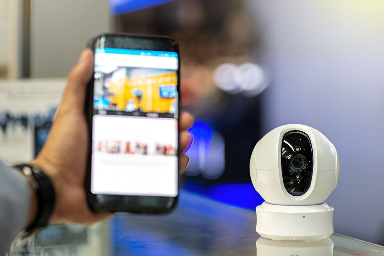 A person is holding a cell phone next to a security camera.