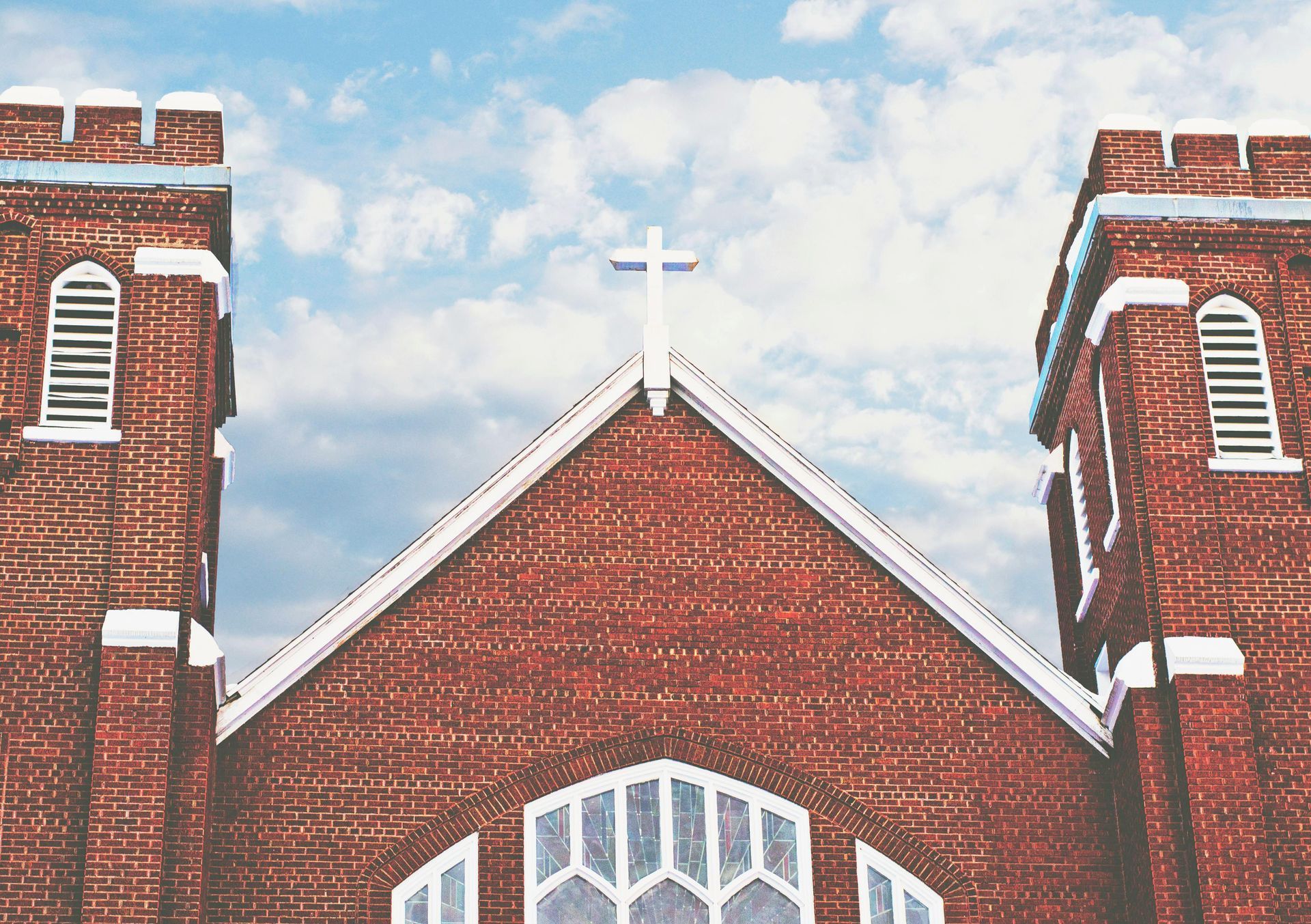 A brick church with two towers and a cross on top of it.