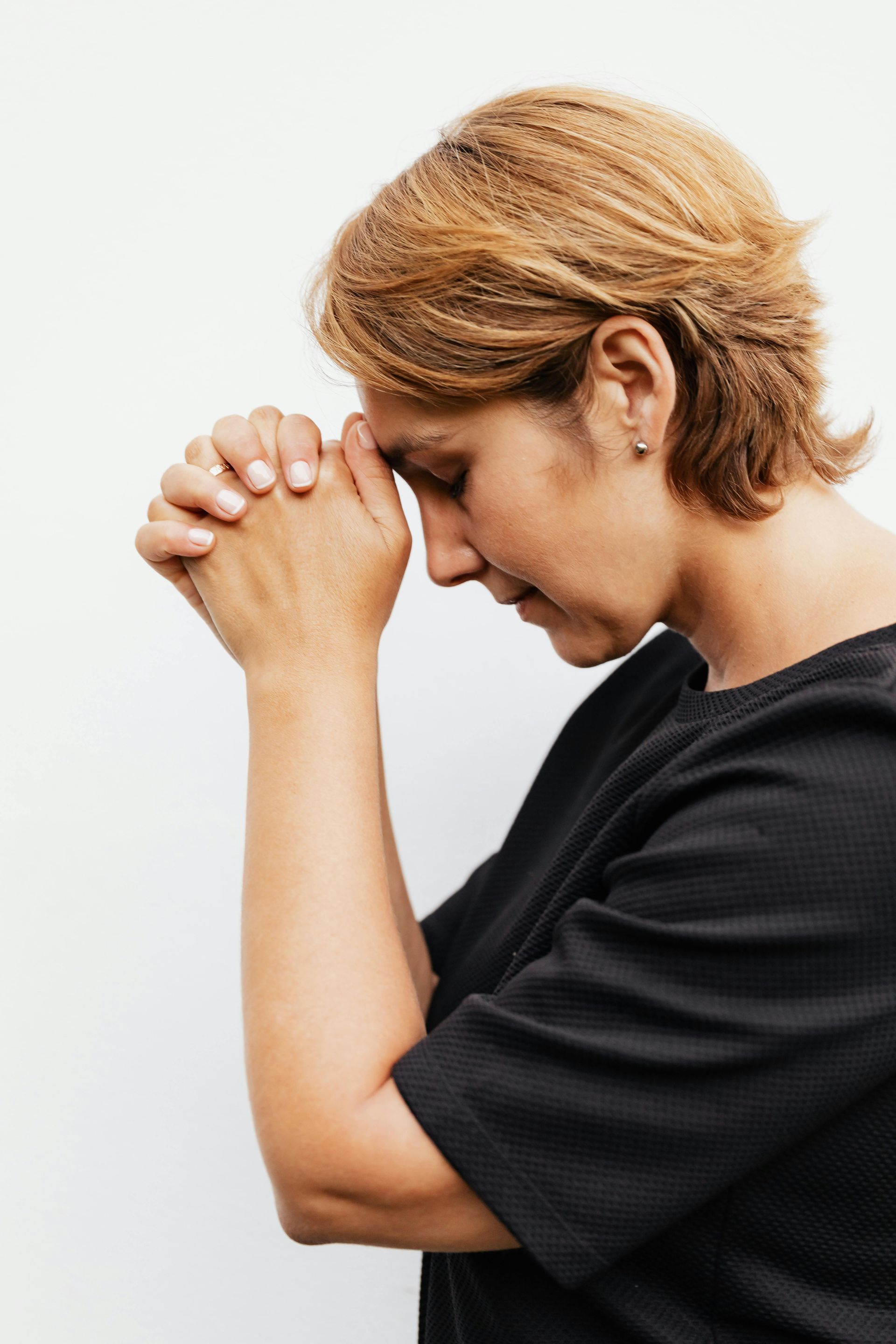 A woman is praying with her hands folded in front of her face.