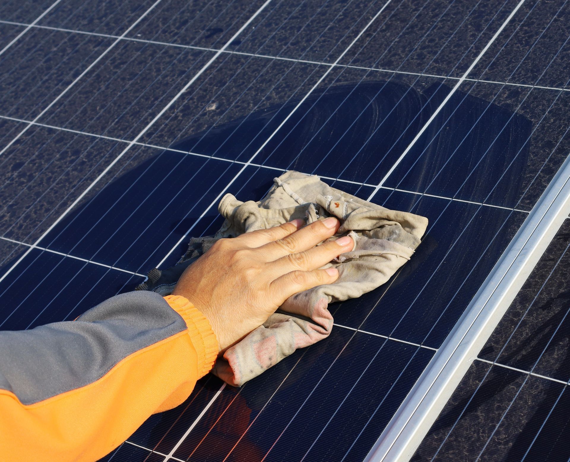 Hand wiping dirt from a dark blue solar panel with a cloth.