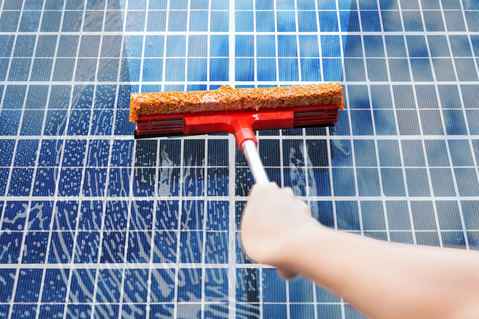 Hand using a red squeegee to clean a blue solar panel surface