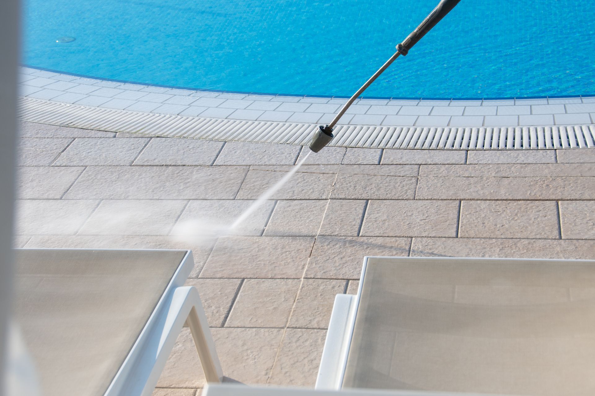 Water spraying across a tiled pool deck near a bright blue pool surface