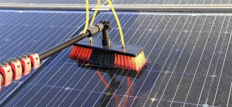 Worker pressure-washing solar panels on a rooftop under bright sunlight