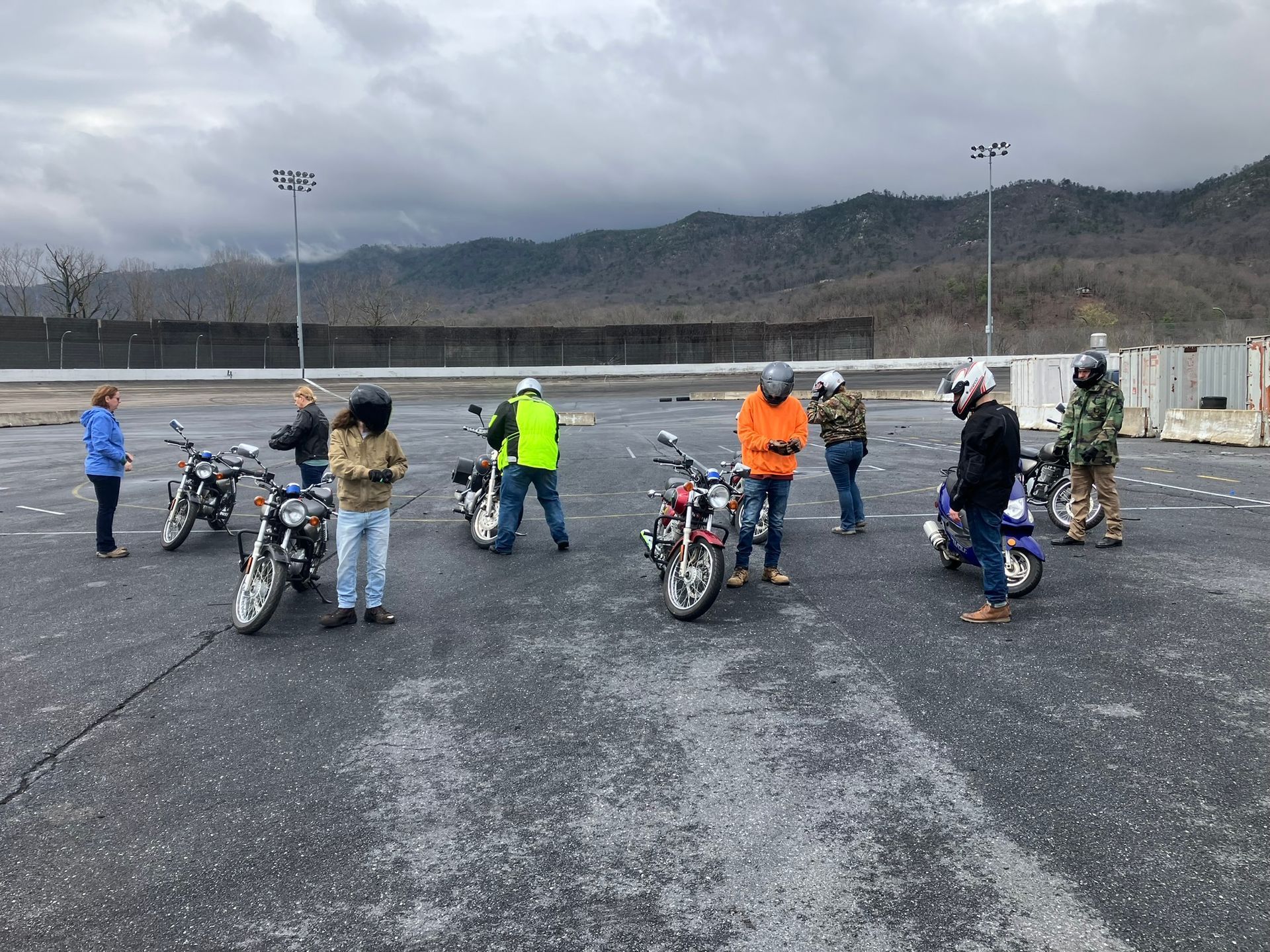 A group of people standing around motorcycles in a parking lot