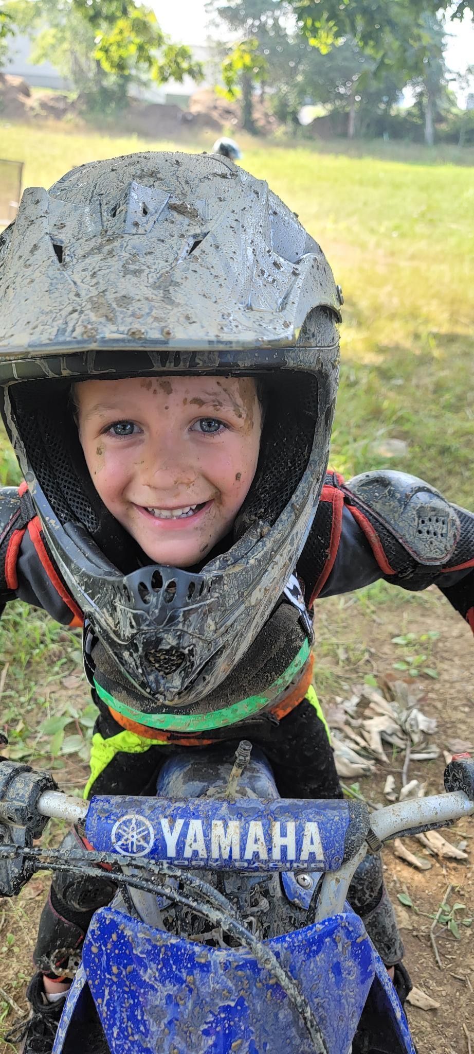 A young boy wearing a muddy helmet is riding a dirt bike