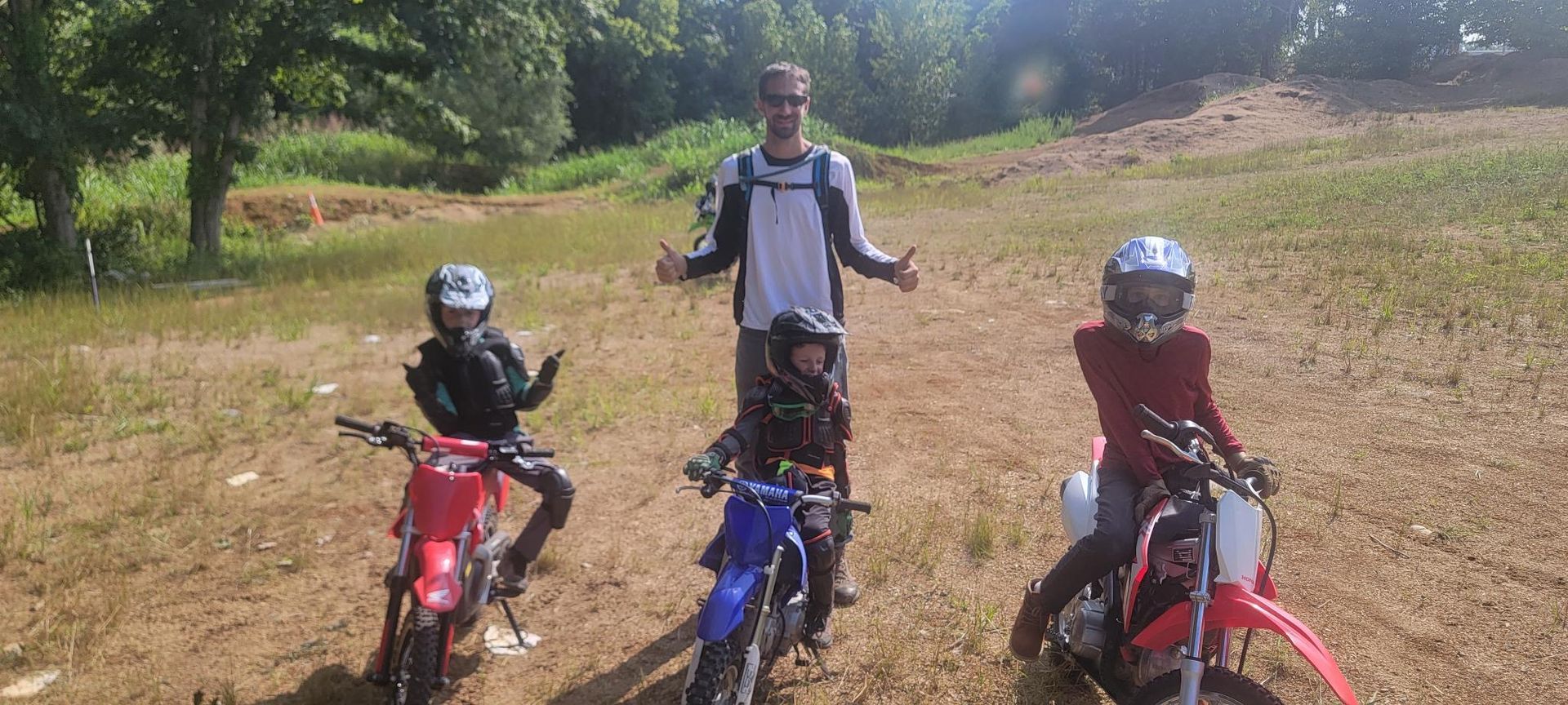 A man and three children are standing next to dirt bikes in a field
